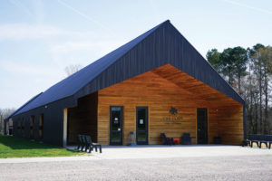 Photo of The Clays at Lone Oaks Farm, a building with black and brown wood exterior in front of a blue sky
