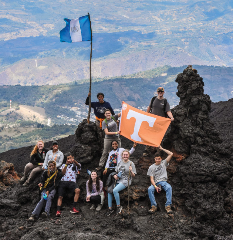 A group of Herbert students holding flags on top of Volcano Pacaya