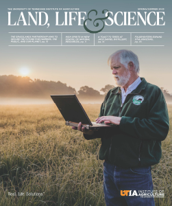 Cover of the Spring/Summer 2023 issue of Land, Life & Science print version, showing Pat Keyser in a native grasslands field while using a laptop.