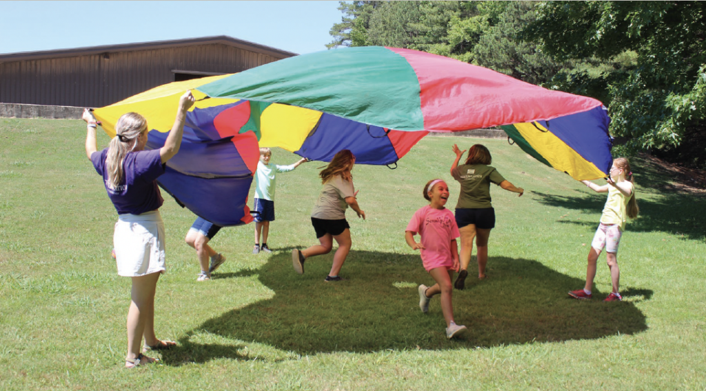 Youth playing in a circle with a multi-colored parachute