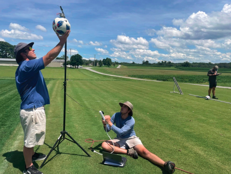 Two students studying the bounce of a soccer ball on turfgrass