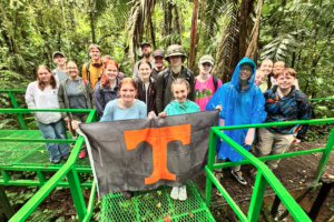 Students in a rain forest holding up a Tennessee Power T flag