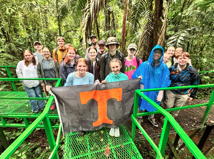 Students in a rain forest holding up a Tennessee Power T flag