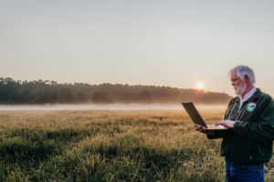 Pat Keyser in a native grasslands field holding a laptop