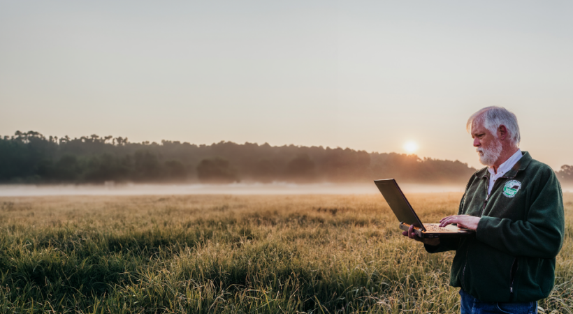 Pat Keyser in a native grasslands field holding a laptop