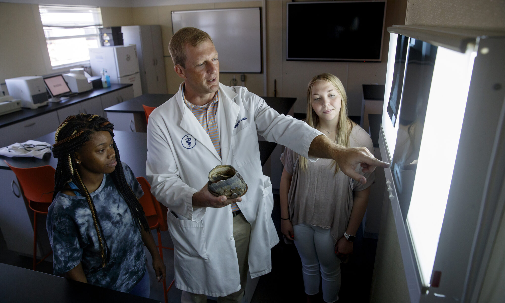 A professor showing two students a hoof compared to a radiograph