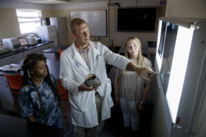 A professor showing two students a hoof compared to a radiograph