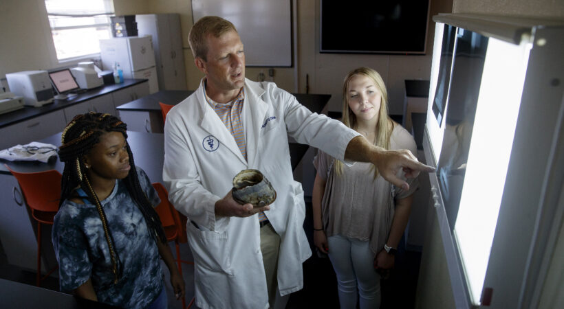 A professor showing two students a hoof compared to a radiograph