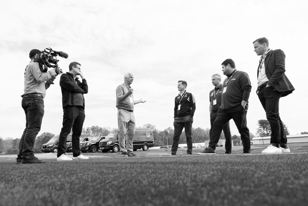 A group of seven people standing together discussing turfgrass with one person holding a camera.