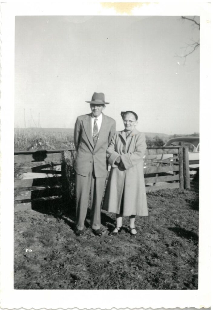 Black and white photo of two people in front of a fence on a farm.