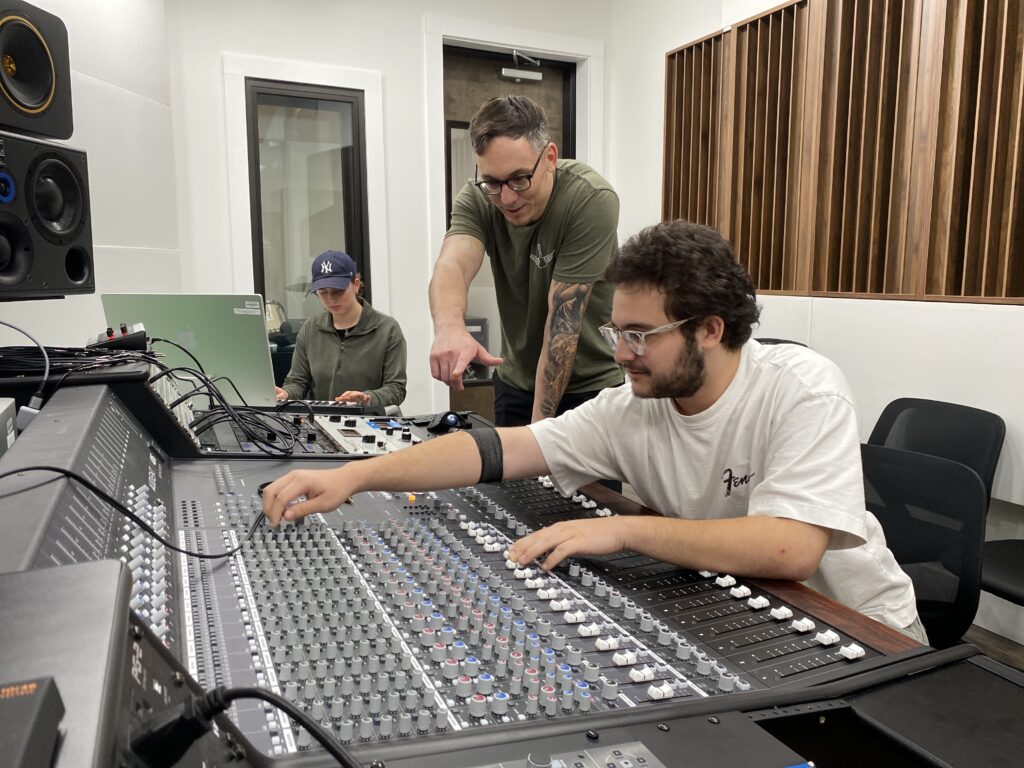 Tyler Reddick helping a student work on a sound board with a second student playing the keyboard.