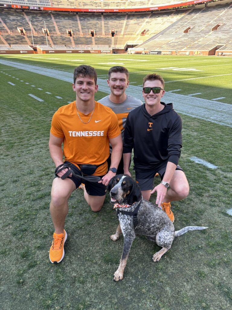 Smokey XII poses with his 2026 handlers, from left, Alex Katzakian, Max Baldwin, and Garrett Reeves following training during the stadium’s first soundcheck.