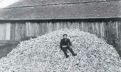 Black and white photo of a person sitting on a high mound of corn