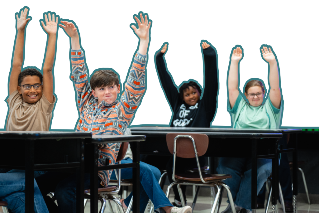 Four students sitting at their desks with both hands raised, participating in a learning activity