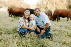 Alyssa Clements, her son, and her husband Adam Boucher posing in a field with cows