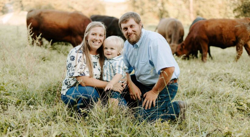 Alyssa Clements, her son, and her husband Adam Boucher posing in a field with cows